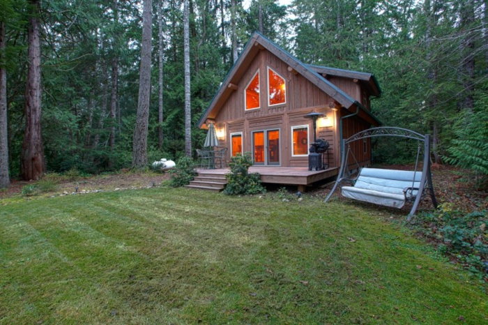 cabañas de madera, prado en el bosque con pequeña cabaña de madera con veranda y escaleras, columpio al lado de la casa 