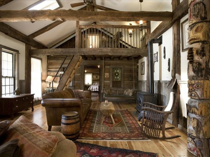 cabañas rurales, grande salón decorado en estilo rústico, escaleras de madera, alfombras y cojines con motivos geométricos, vigas de madera en la pared