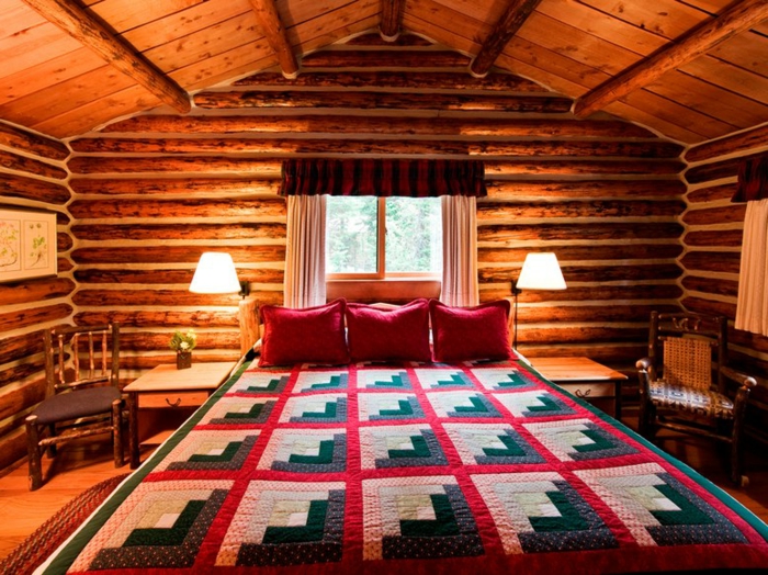cabaña de madera, habitación acogedora, cama doble con cobija de lana, paredes y techo de madera, cojines decorativos en rojo