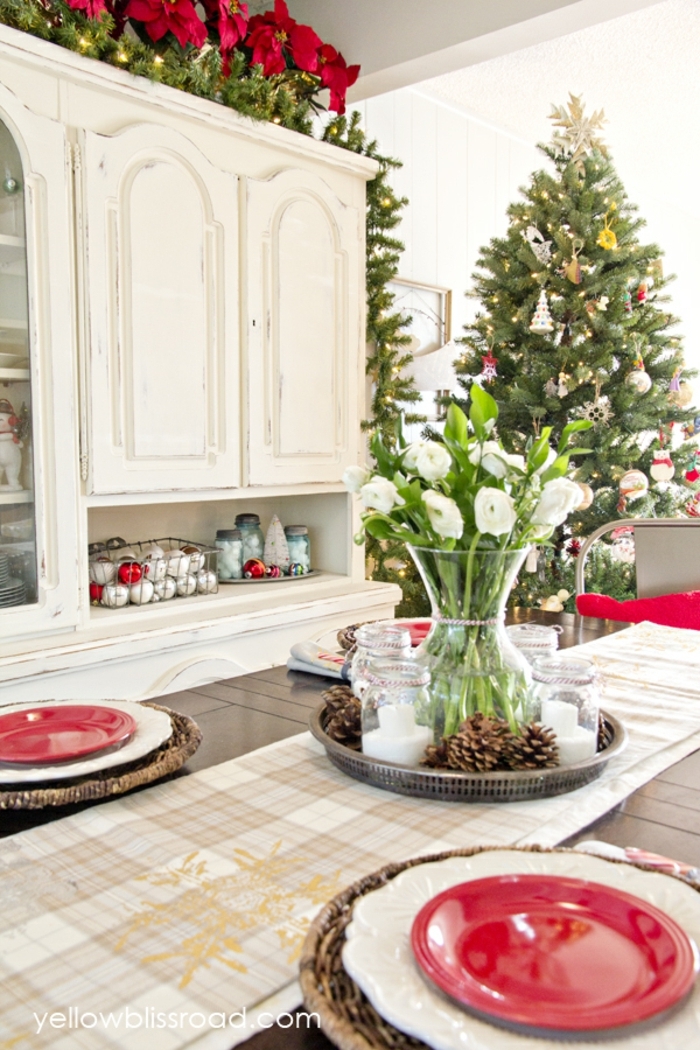 centros navideños. comedor estiloso en colores claros, centro de mesa de flores y piñas, platos en rojo 