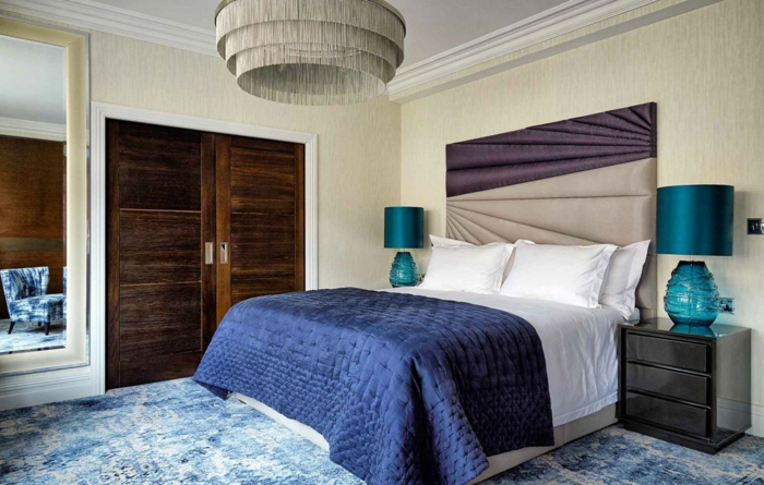 dormitorio matrimonio, habitación en tonos fríos, puerta de madera, lámpara de araña interesante y suelo de moqueta en azul y blanco 
