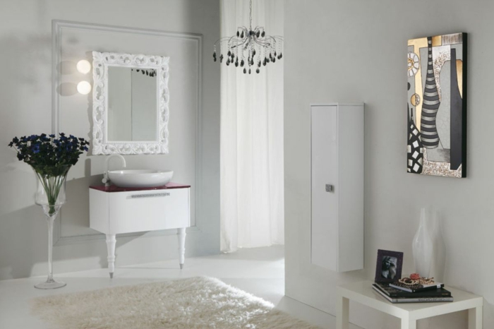 baños modernos, baño con alfombra, todo blanco. lámpara de araña, pintura nature morte como acento, espejo con marco grande