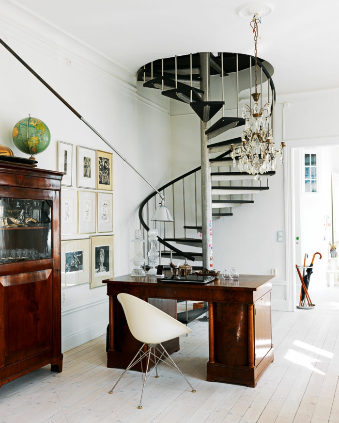 escaleras, salon con escritorio de madera, suelo con tarima blanca, escaleras negras de caracol con barandilla, lampara de araña