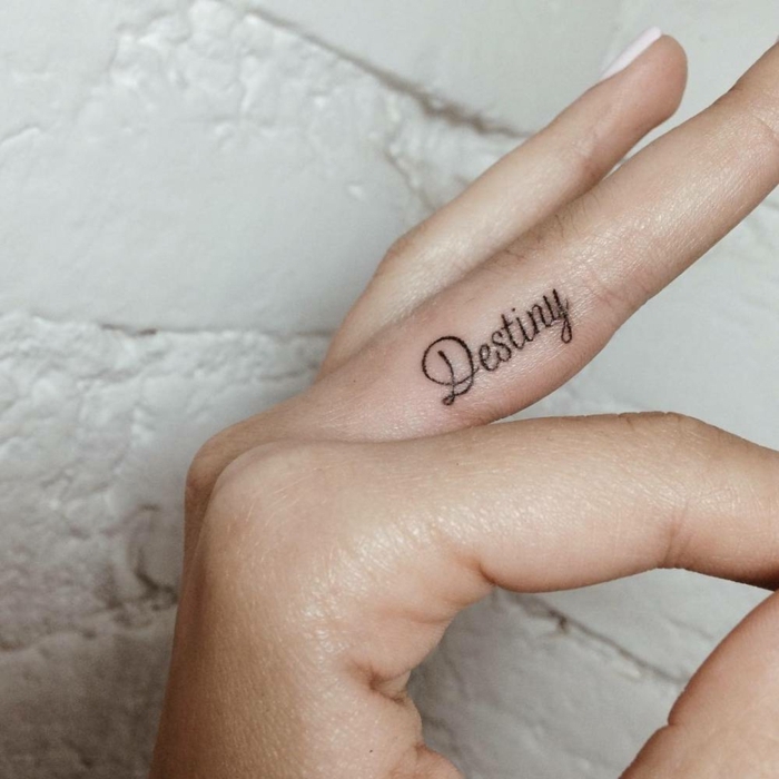 tatuajes en la mano, mano de mujer, tatuaje de frase en cursiva sobre la parte lateral del dedo cordial, idea de tatuaje femenino