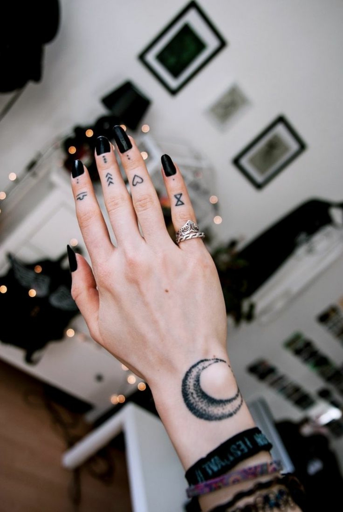 ideas para tatuajes, mano de mujer con uñas largas negras, tatuaje de luna en la muñeca, corazón y flecha en los dedos