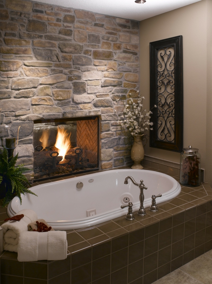 pared de piedra, decoración de baño con chimenea encendida y bañera, pared de piedra rústica y flores
