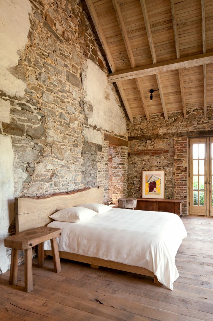 paneles decorativos, dormitorio grande con cama doble, estilo rústico, cabecero de madera, techo con vigas, paredes de ladrillo con aspecto desgastado