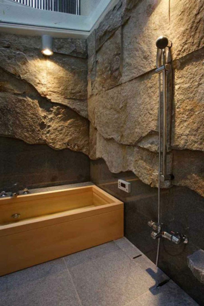 paredes decoradas, baño con bañera de madera y ducha de mano, pared de piedra decorativa, luz artificial