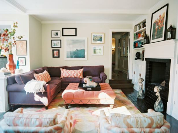 habitacion vintage, mesa baja tapizada en capitoné, sofá grande en color lila, mucha decoracion en las paredes
