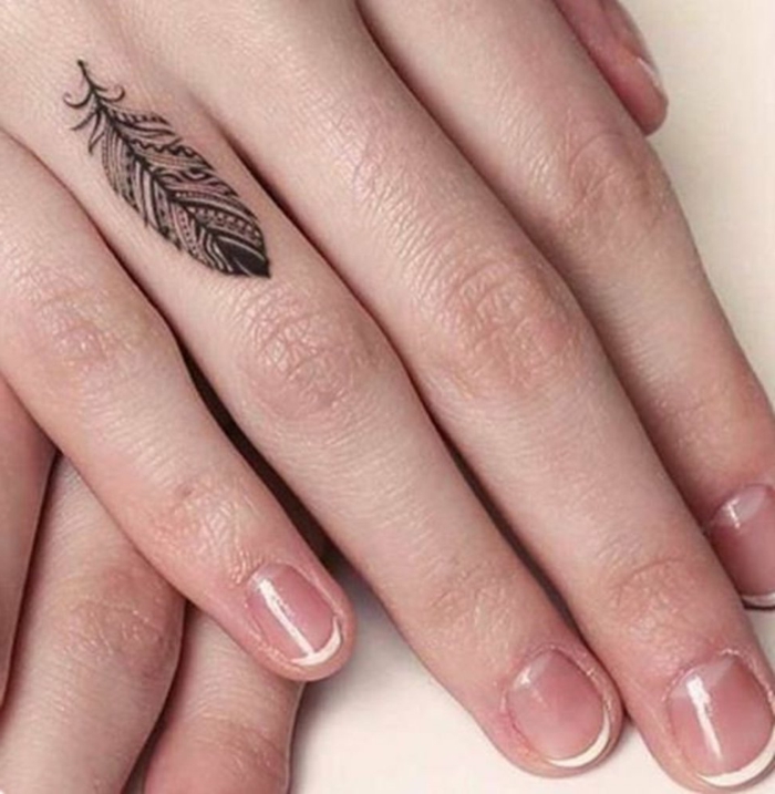 tatuajes en la muñeca, mano de mujer con manicura, tatuaje minimalista en el dedo anular, pluma negra