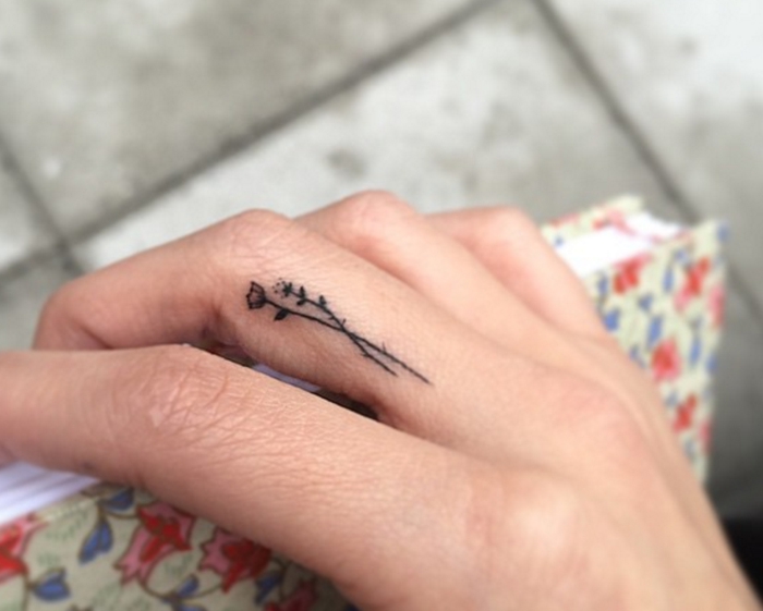 ideas para tatuajes, tatuaje en la parte lateral del dedo corazon, mano de mujer colgando un libro, tatuaje minimalista femenino