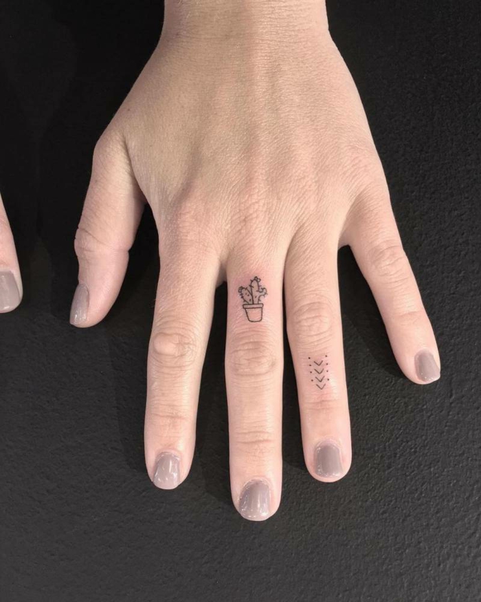 tatuajes en la muñeca, mano de mujer, idea de tatuaje con cactús en el dedo medio y flechas en el anular