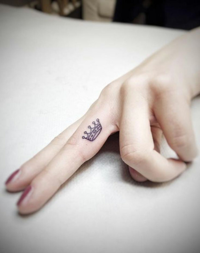 tatuajes en la muñeca, tatuaje minimalista femenino en la parte lateral del dedo medio, pequeña corona
