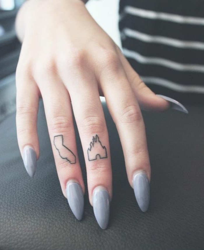 tatuajes en la mano, mano de mujer con manicura gris, dedo medio y dedo anular con tatuajes del castillo de Disney y el mapa de California