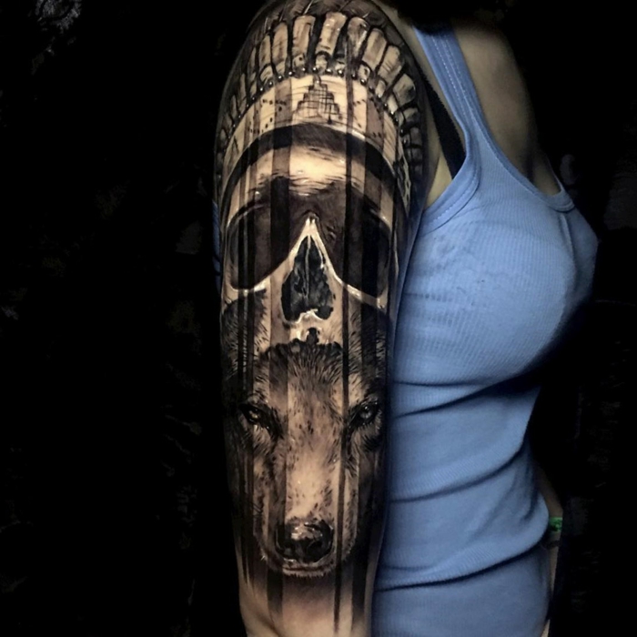 tatuaje ant5ebrazo mujer, mujer con blusa azul con tatuaje grande negro, cabeza de lobo y calavera, estilo surrealista