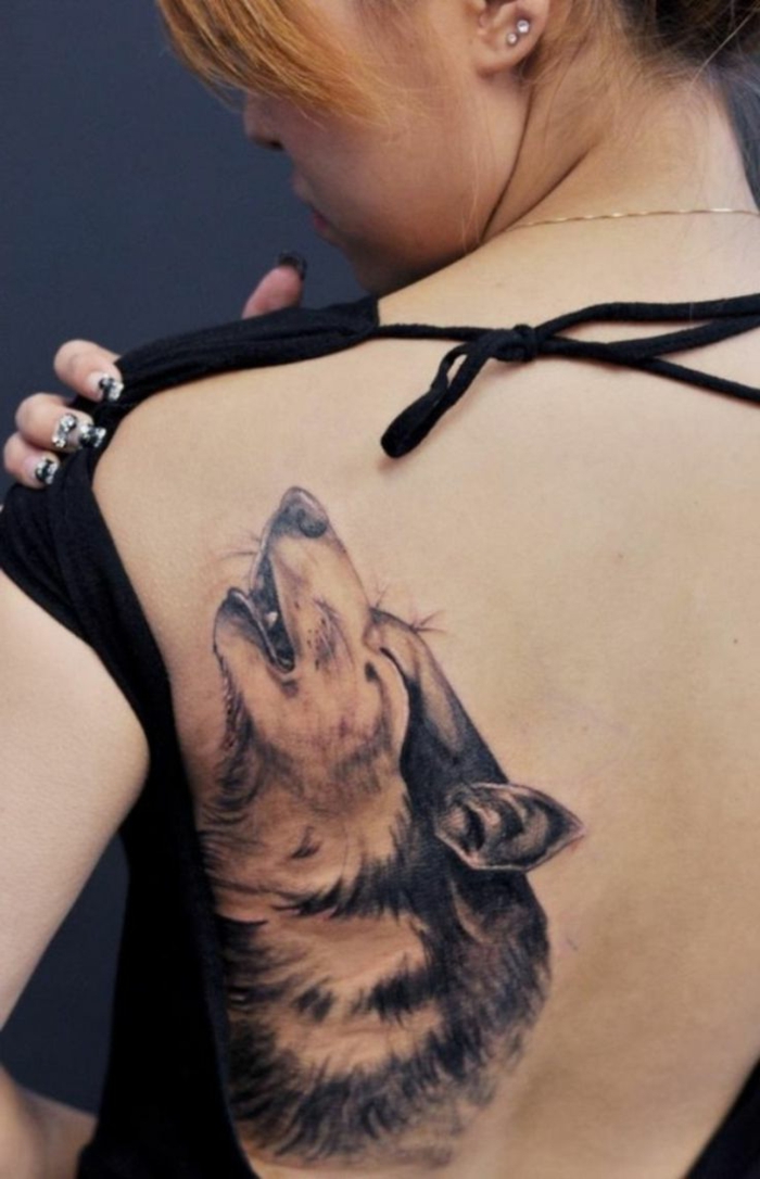 tatuaje geometrico, mujer con pelo corto y blusa negra, tatuaje en la espalda, cabeza de lobo estilo realista