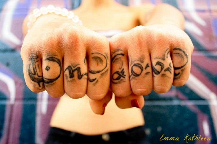 tatuajes en la mano, mujer con los puños cerrados y pulsera, tatuaje con frase en los dedos, one love