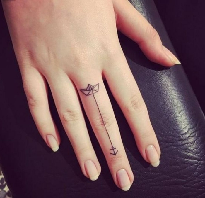 tatuajes dedo, mano de mujer, tatuaje minimalista con barca de papel y flecha negra en el dedo corazón