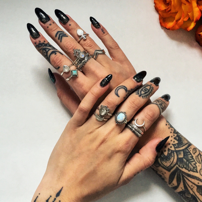 tatuaje corazon, manos de mujer con uñas largas negras, muchos anillos, tatuaje en la muñeca y los dedos, la luna, el ojo de la providencia