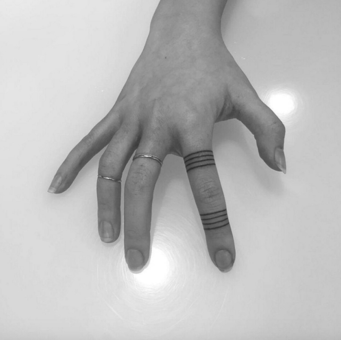tatuajes mujer, mano de mujer con anillos de plata, índice con tatuajes negros tipo anillo, foto en blanco y negro
