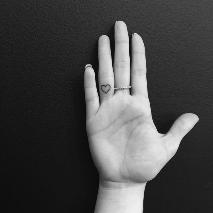 tatuajes en los dedos, foto de mano de mujer en blanco y negro, tatuaje con corazon pequeño en la parte anterior del dedo anular