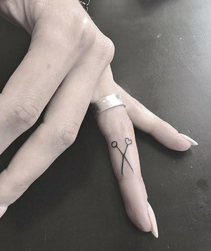 tatuajes en los dedos, tatuaje minimalista con tijeras en el dedo anular, mano de mujer con manicura y anillo de plata