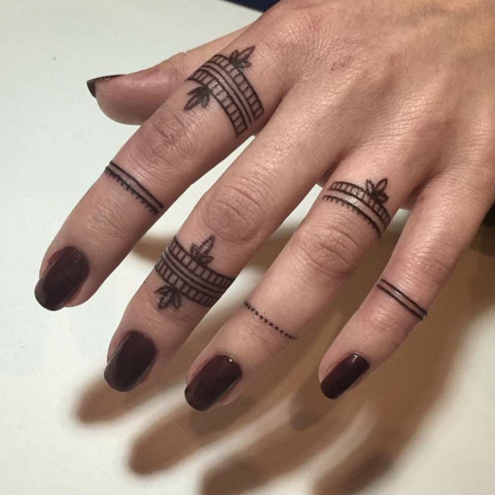 tatuajes en los dedos, mujer con uñas en carmín, dedos con tatuajes negros de anillo diferente tipo