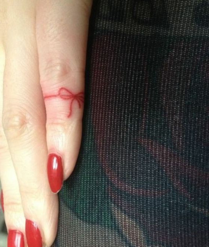 tatuajes en los dedos, mano de mujer con manicura, uñas rojas, tatuaje minimalista en el menique, lazo rojo