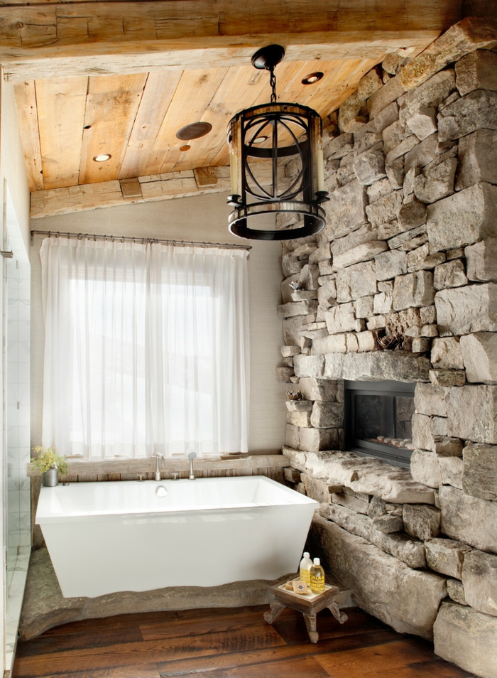 ejemplo acogedor de baño rústico con bañera moderna, baños rusticos abuhardillados, pared de piedra natural con chimenea empotrada