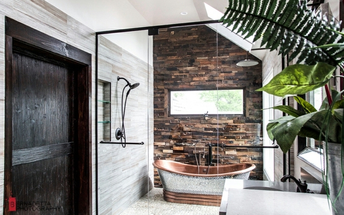propuesta moderna de un baño con decoración con elementos rústicos, bañera en marrón u plata, pared de piedra y decoración de plantas verdes