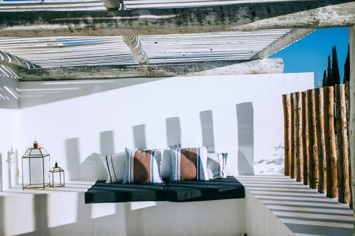 terraza atractiva en blanco con elementos de madera, cojines decorativas, techo de vigas de madera, sitio para relax