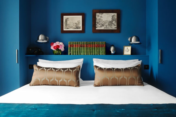 dormitorio en estilo vintage con decoración de cuadros, jarrón con flores, cojines decorativos y paredes pintadas en azul saturado