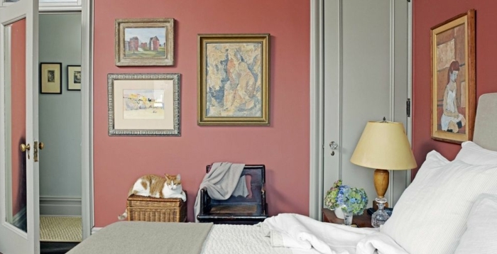 cuarto pequeño con cama doble, paredes pintadas en color salmón y preciosa decoración de cuadros clásicos