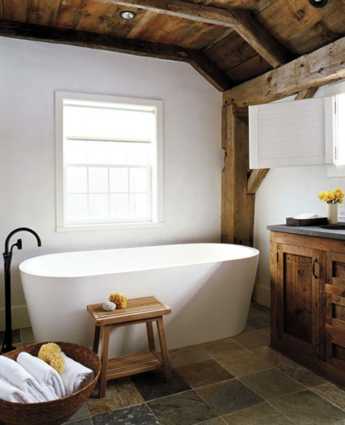 elementos típicos para un baño con decoracion rustica, bañera moderna exenta, paredes con vigas de madera y techo de madera con lámparas empotradas