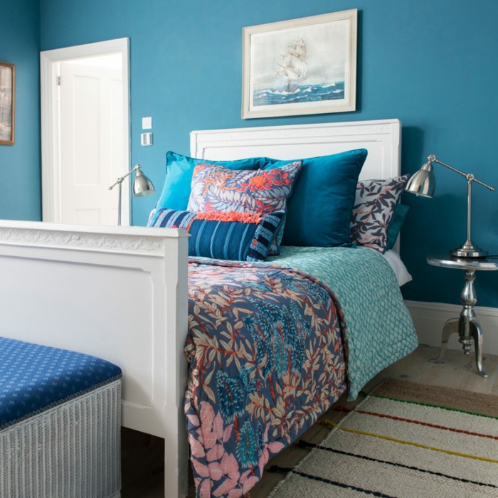 cama individual de madera pintada en blanco con cabecero, paredes pintadas en azul turquesa y decoradas con cuadros modernos