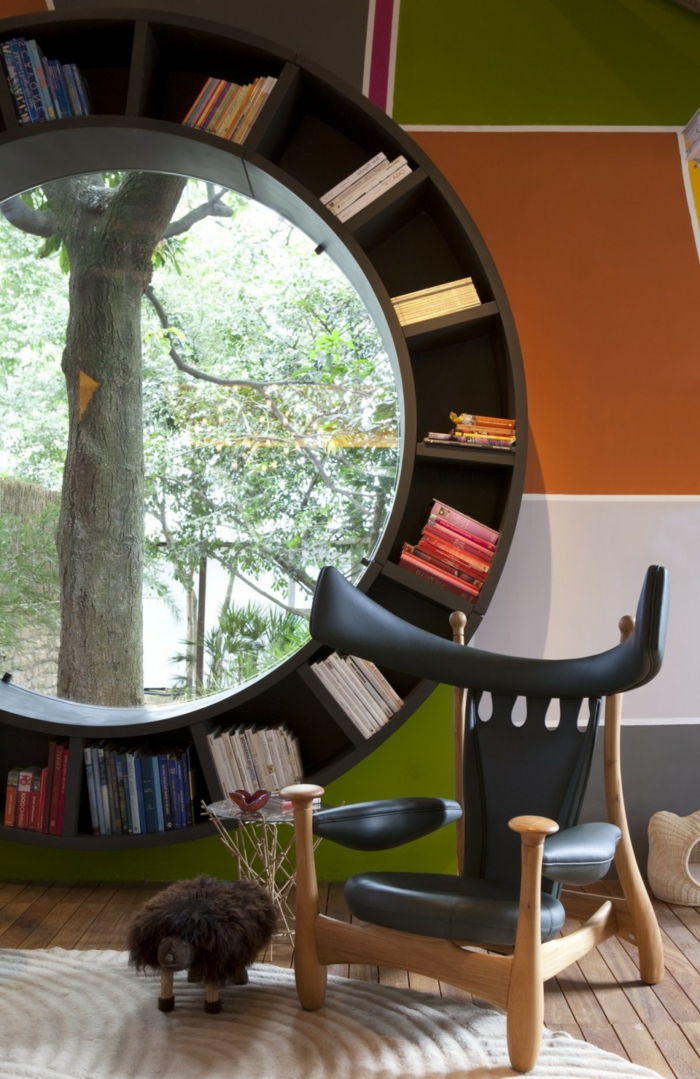 estanterias para libros, idea de librería redonda con ventana, silla moderna de madera y piel, tapete, suelo con tarima, pared en cuadrados de color, naranja, verde y gris+