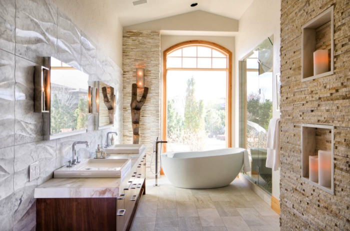 baño con luz natural, decoración moderna, muebles auxiliares, paredes de piedra, bañera ovalada, lavabo doble con espejos grandes