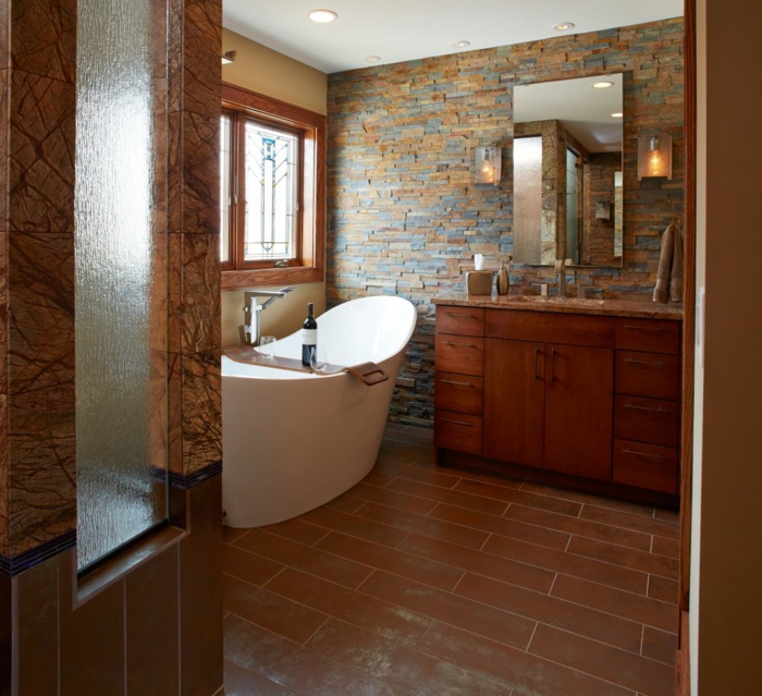 cuartos de baño rústicos con toque moderno, paredes de ladrillo en diferentes tonos terrosos, suelo de azulejos en marrón y bañera exenta