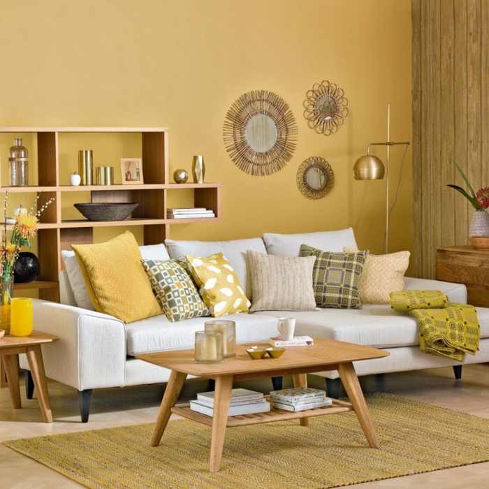 sala de estar decorada estilo moderno, colores para paredes, idea en color mostaza con sofá blanca con cojines, decoración con espejos, mesa de madera, tapete de mimbre