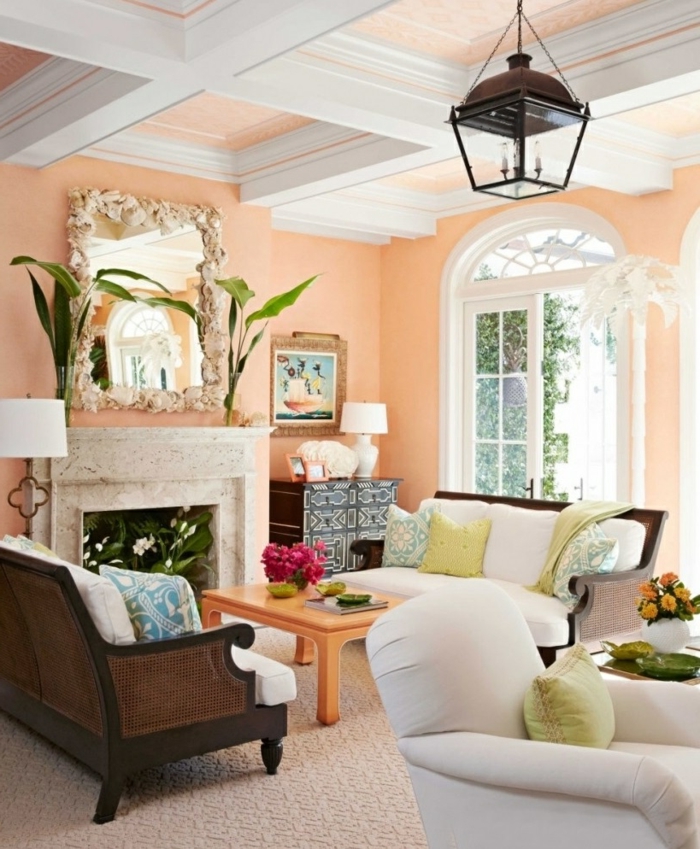 salón con paredes en color melocoton, pintura para paredes, espejo grande, chimenea decorada con plantas, lámpara tipo linterna, ventana grande, mesita coolor naranja, sofá tapizado blanco