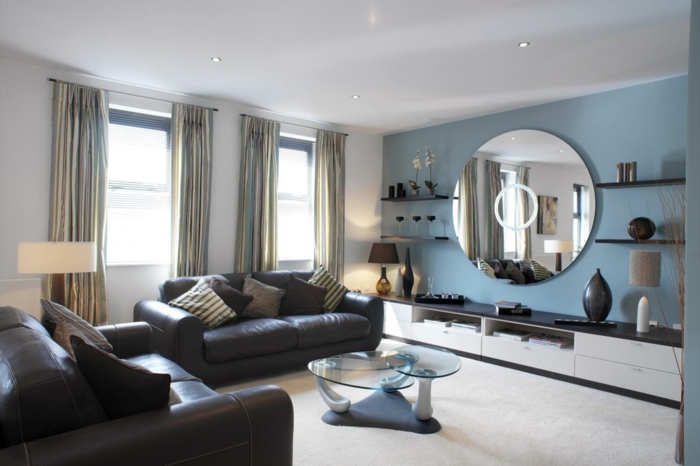 ideas de decoracion moderna, colores para salones, pared de acento en azul, sofás de piel con cojines, espejo grande redondo, ventanales con cortinas
