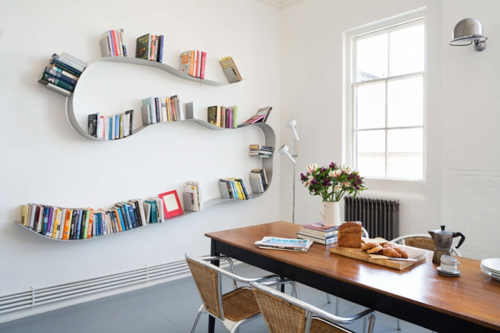 librería moderna de metal en forma de serpiente, estanterias originales, comedor con mesa de madera, paredes blancas