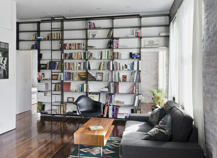 estilo contemporaneo, librería de suelo a techo color negro con escalera movible, mesa de madera, sillón de plástico, sofá gris, baldas de madera