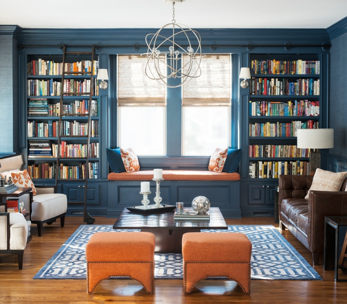 salón clásico, decoración en color naranja y azul, librería de madera azul, ventana con banco con colchoneta y cojines, alfombra. sofá de piel, estanterias para libros