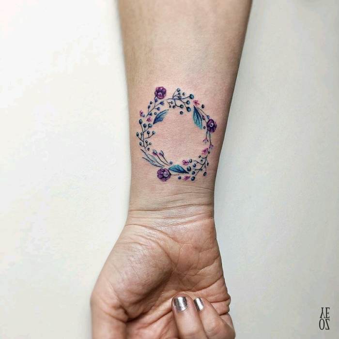 tattoo en la muñeca, tatuaje femenino de color, corona de flores y hojas en lilá y azul, uñas con esmalte plateado