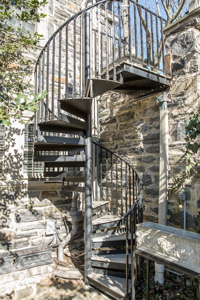 escaleras de madera, patio con muro de piedra y plantas verdes, escalera de caracol de metal con barandilla