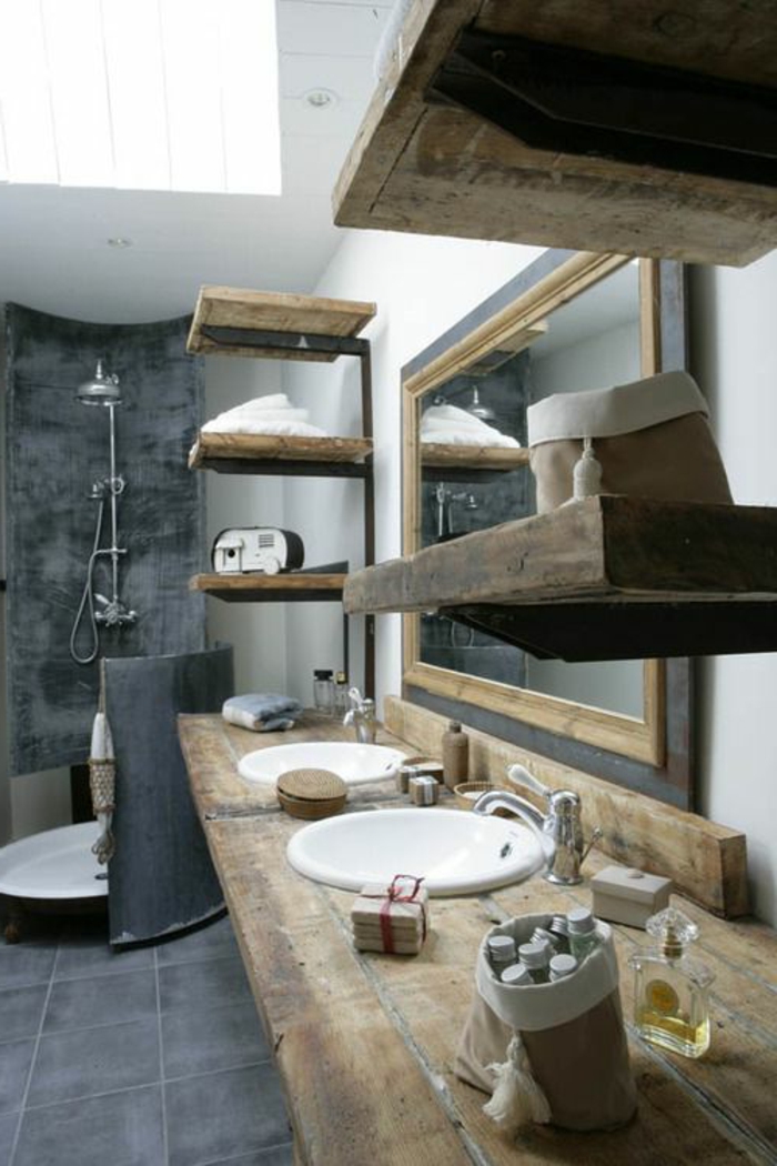 cuartos de baño rusticos con estanterías de madera, paredes de hormigón y suelo con bañdosas en gris, grande espejo con marco de madera