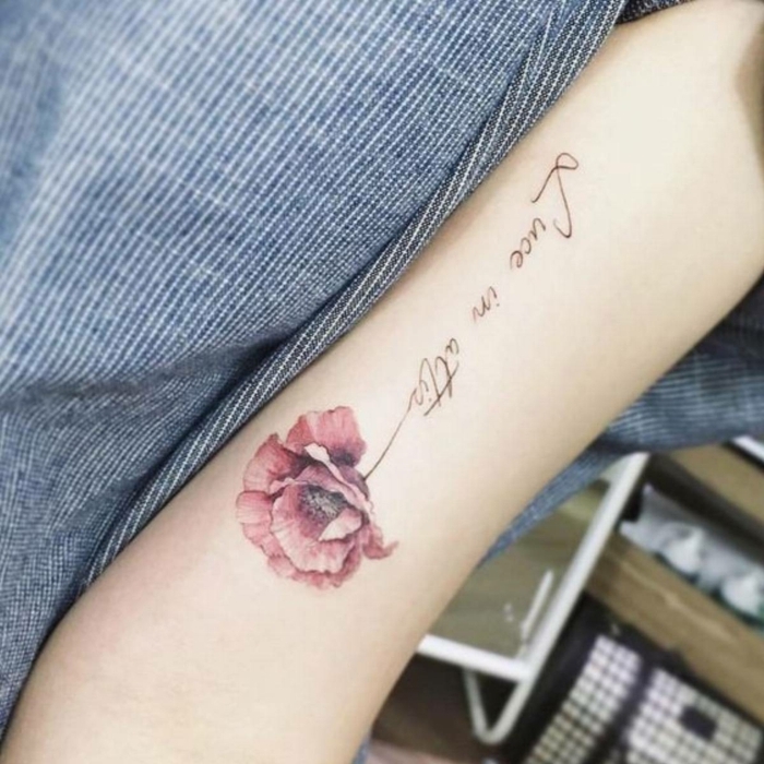 tatuaje acuarela, tatuaje femenino en la parte interna del brazo, amapola roja con tallo con frase en cursiva negro