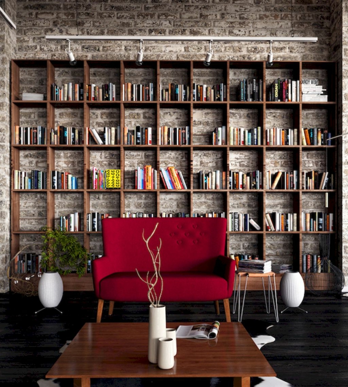 salón con ladrillo visto, estanterias de pared, librería grande de madera, sillón tapizado rojo, elementos vintage, planta verde, maceta blanca