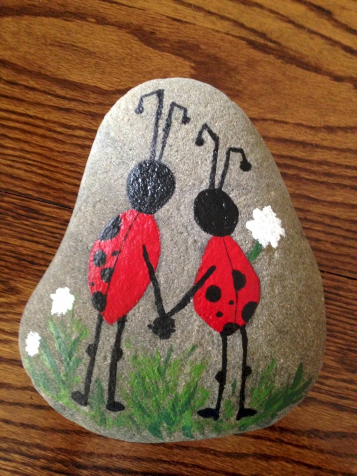 pintar con acrilico, piedra natural, dibujo de mariquitas con dos piernas agarrados de la mano, flores blancos, idea para niños